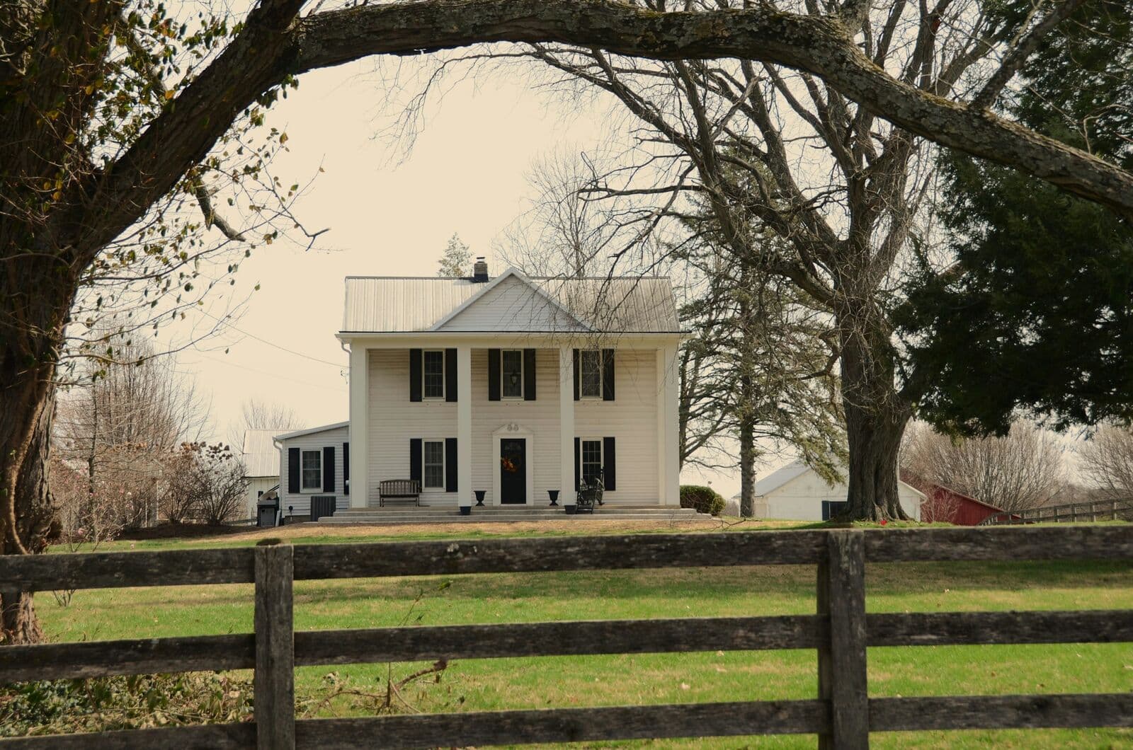 White farmhouse with a columned porch behind a board fence